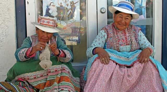 Two older women sit on a stoop in Chivay, Peru wearing traditional costumes.