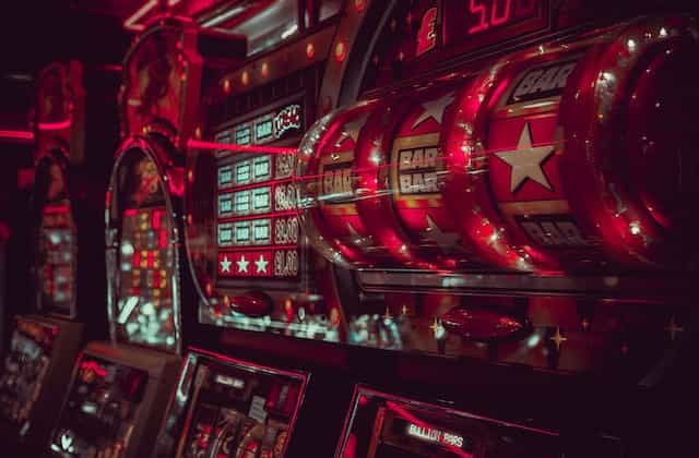 A series of classic roulette machines drenched in neon red light inside of an indoor retail casino location.