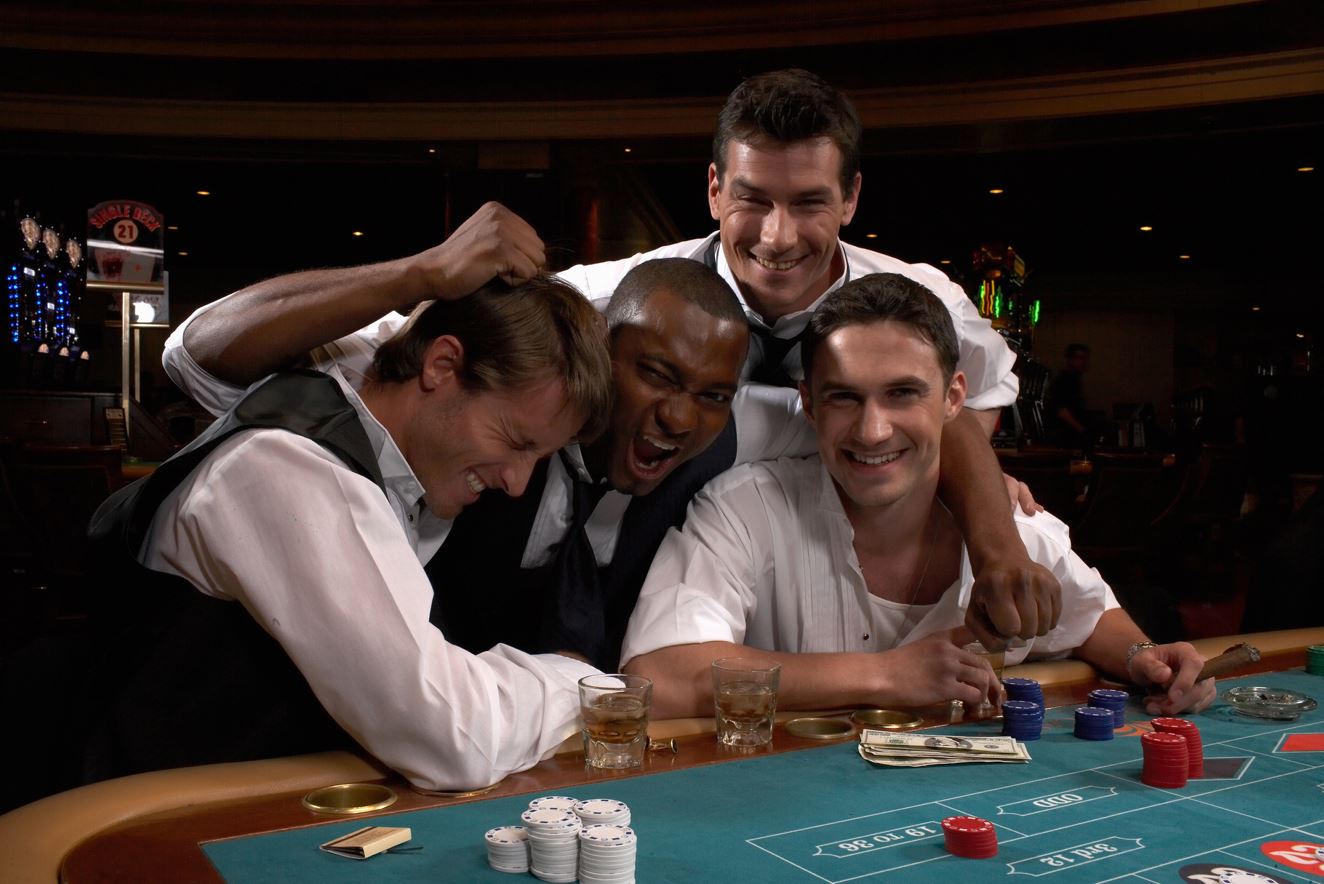 Four men sat in casino playing roulette while having fun and looking happy.